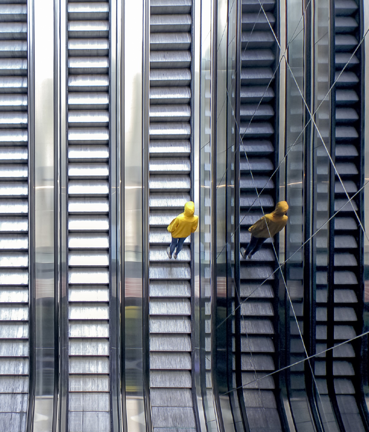 Person in a yellow hooded jacket rides an escalator