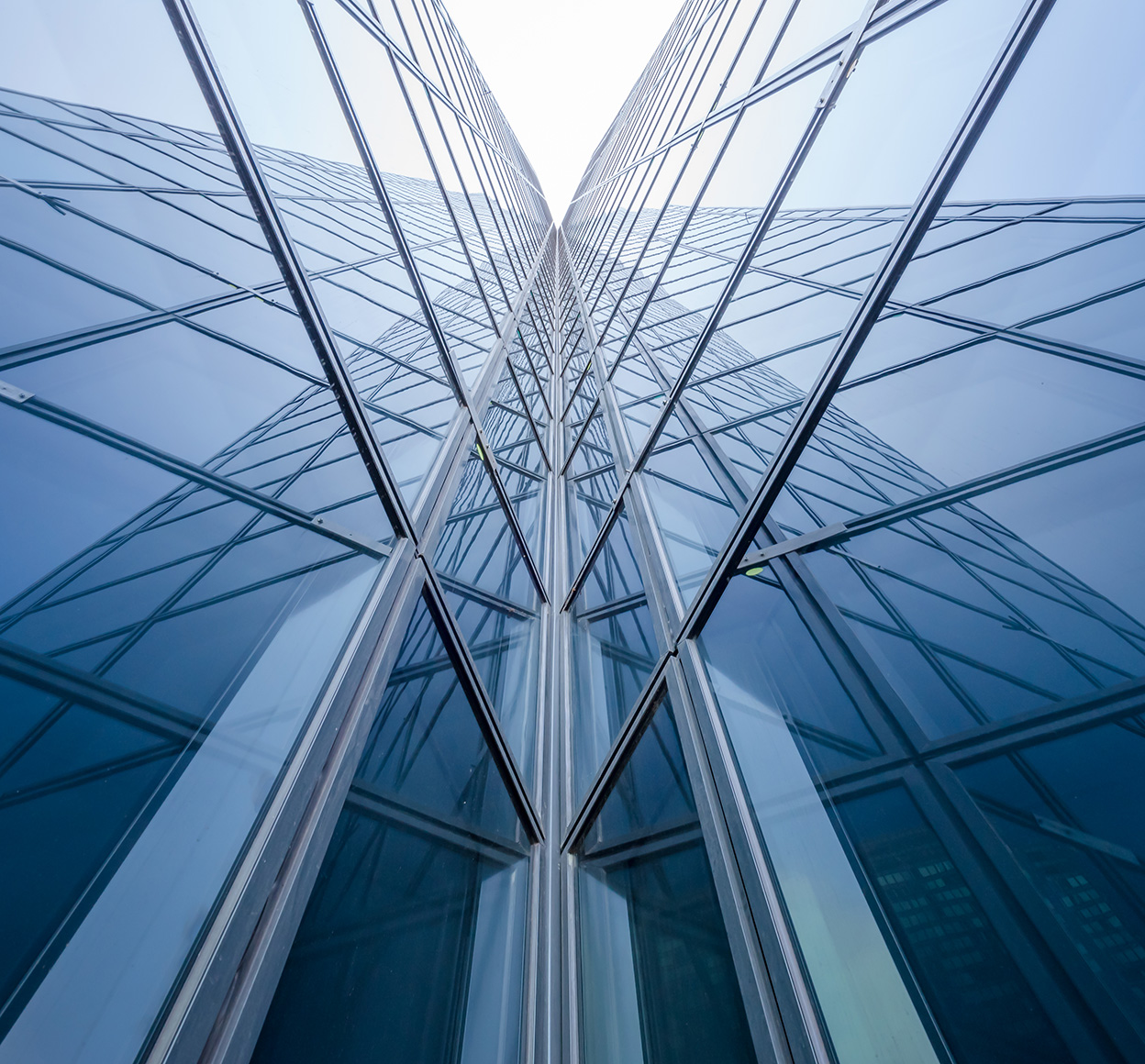 This image is a stunning close-up of a tall, sleek, blue glass building that reflects the blue sky and creates mirror reflections against the sky.